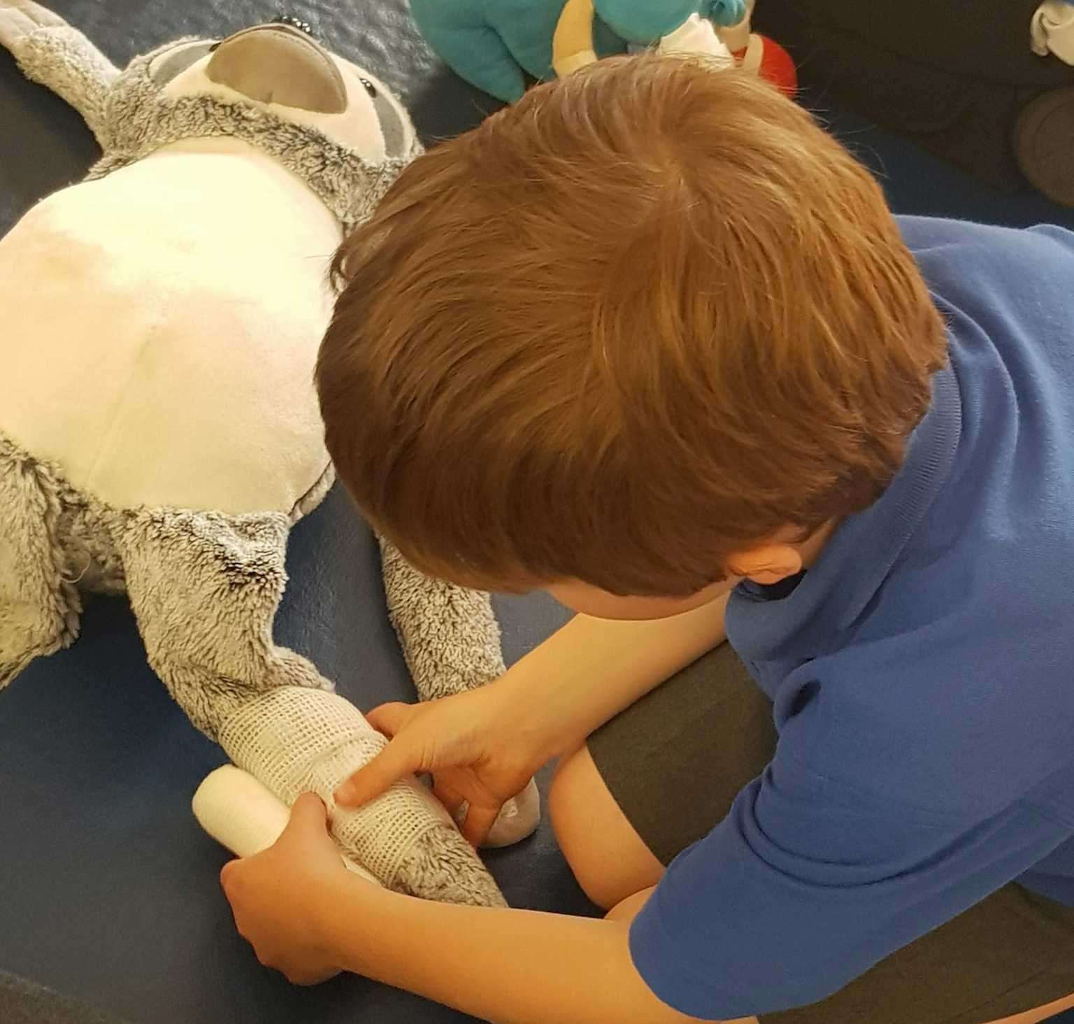A pupil tries their hand at bandaging on a soft toy patient