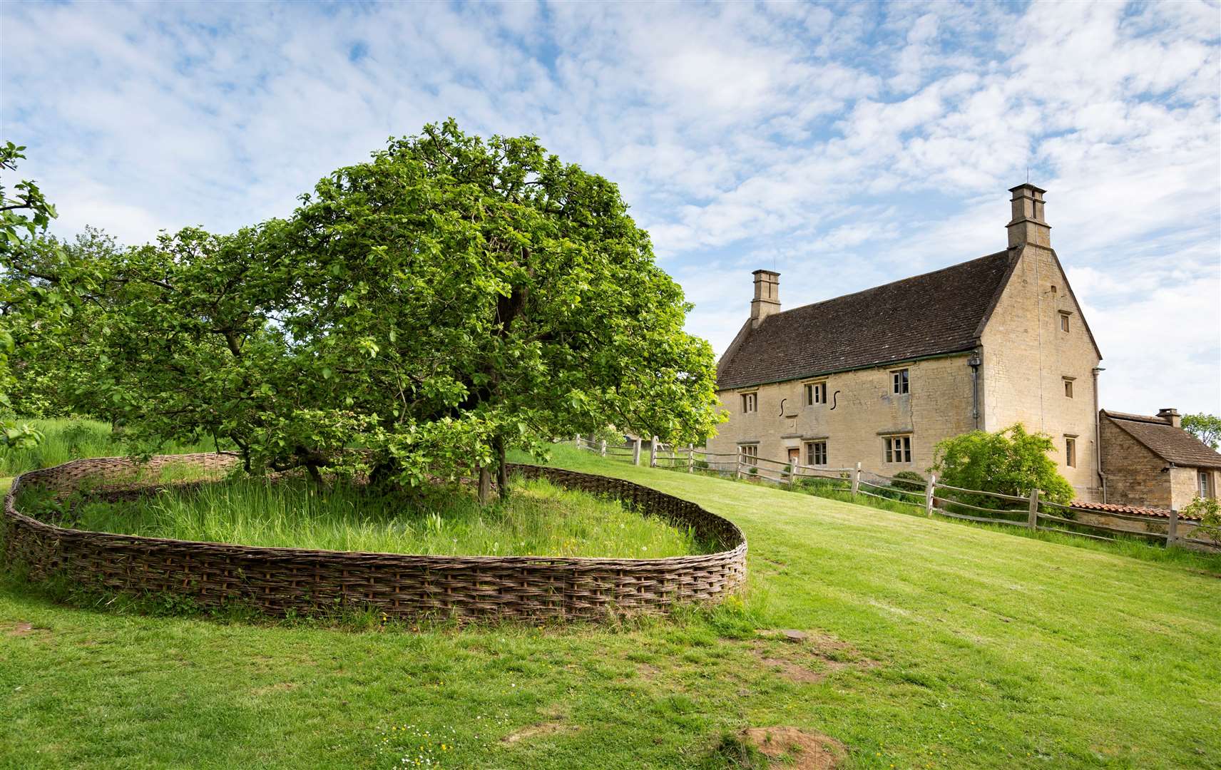 Isaac Newton's apple tree protected by willow fence in the garden with the farmhouse at the background at Woolsthorpe Manor, Lincolnshire. Woolsthorpe was home to the world-famous scientist and mathematician Sir Issac Newton.