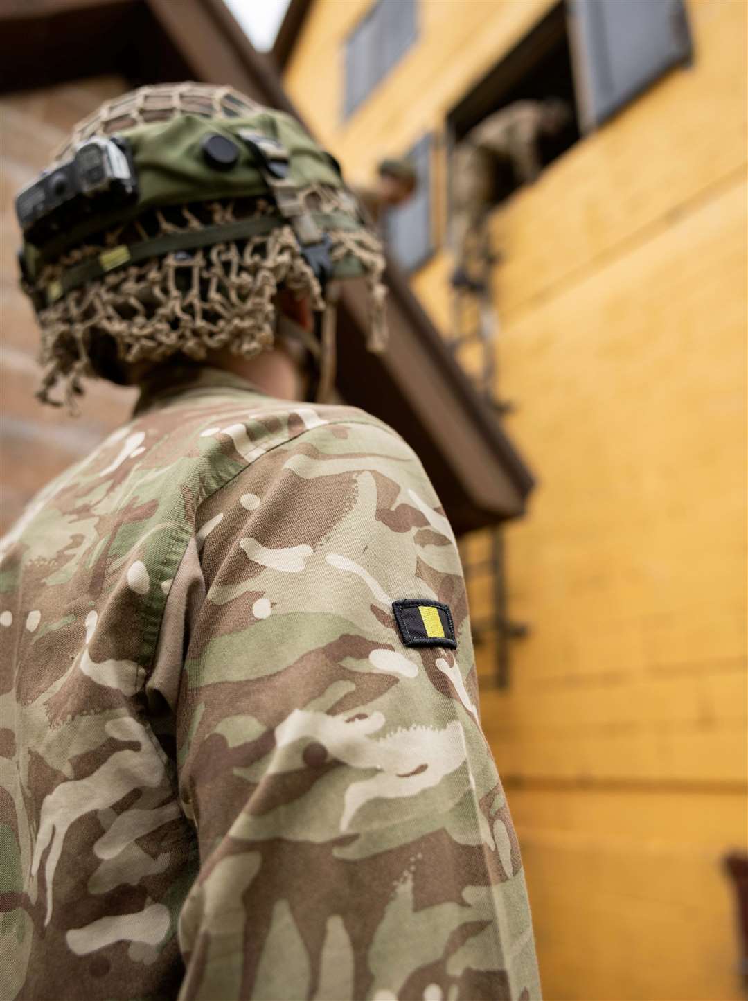 A soldier watches his colleagues climbing into a house.