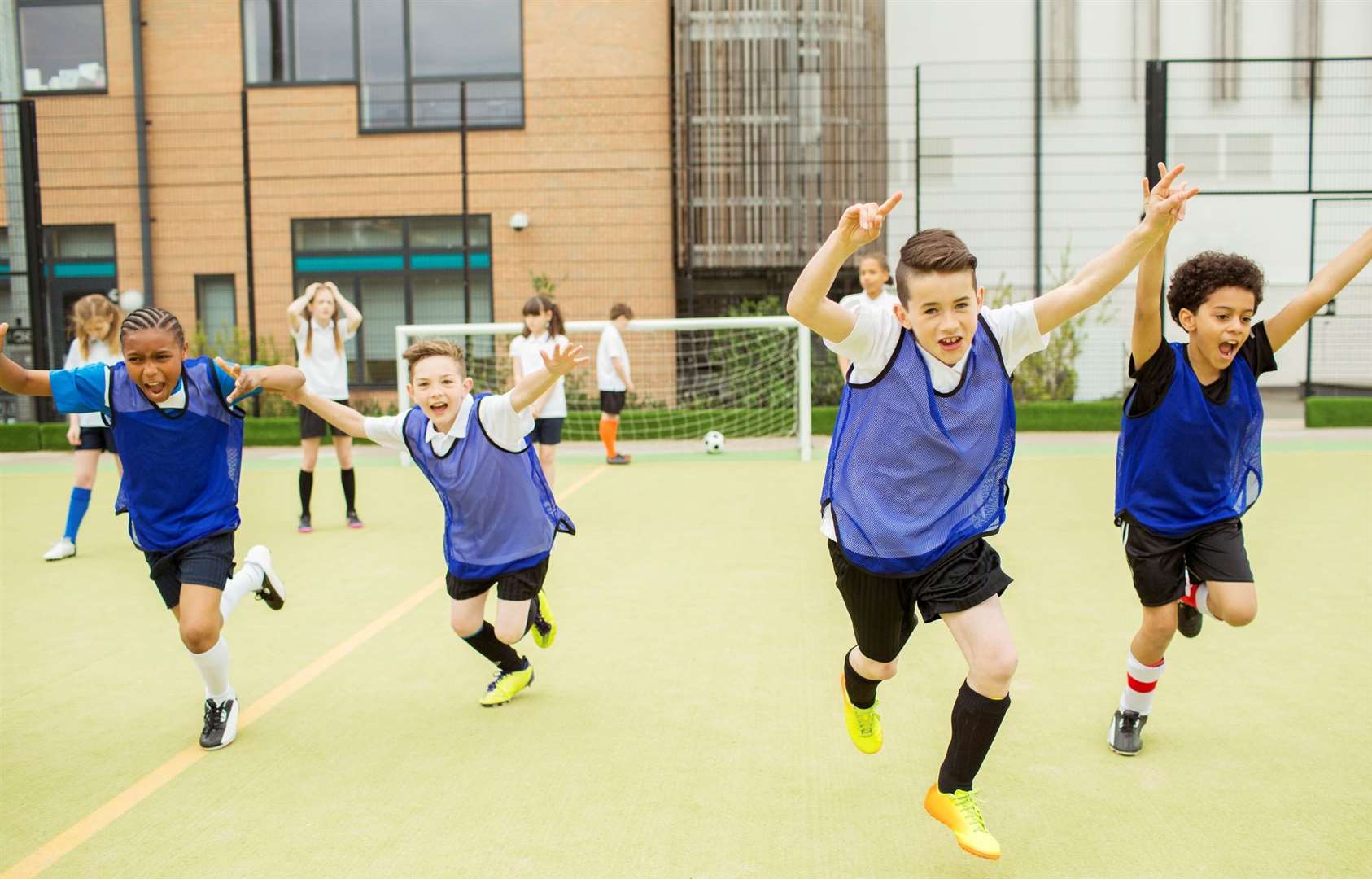 Schoolboys wearing sport uniforms running with arms raised in soccer field in front of school. Photo: istock