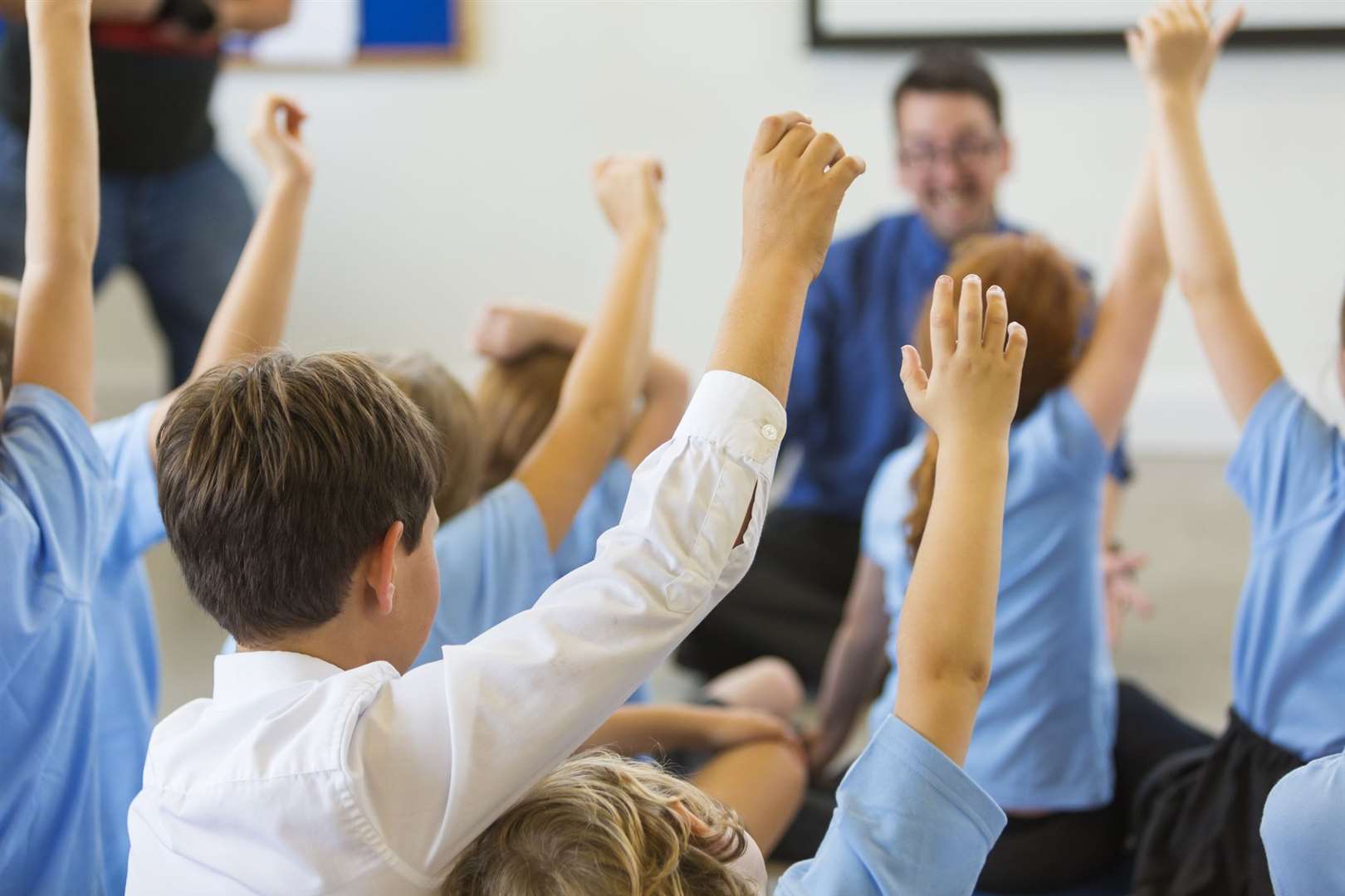 Excited school children in school uniform with hands up ready to answer a question from the teacher. Stock image