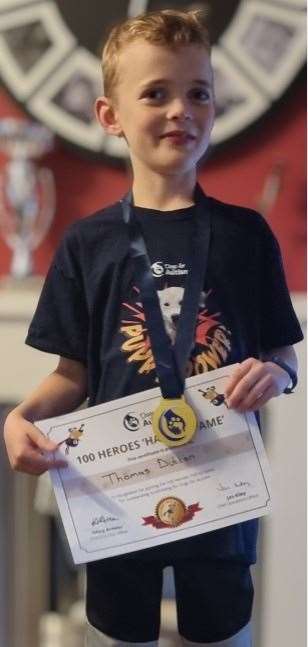 Thomas Dutton, 8, with his '100 Heroes' certificate and medal from the Dogs for Autism charity.